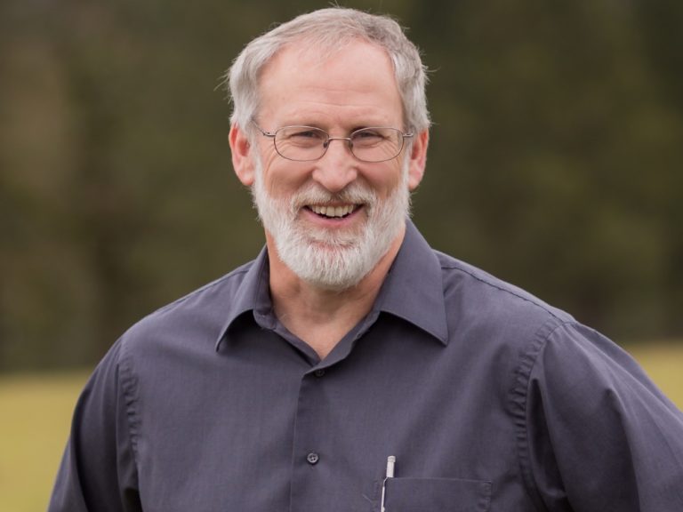 Smiling gray-haired man with glasses and beard outdoors