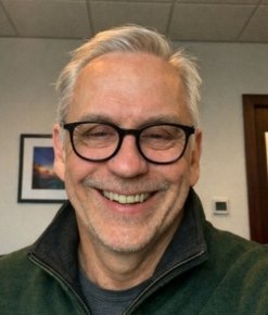 Smiling gray-haired man wearing glasses and a dark jacket